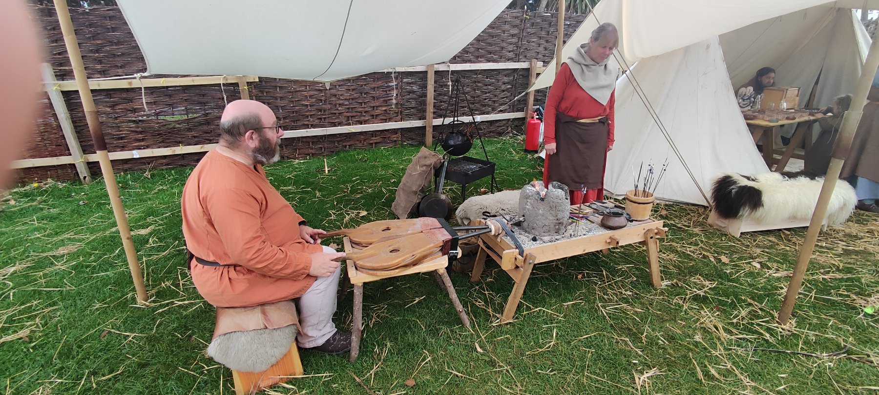 A blacksmith working at a small portable forge inside the Viking encampment